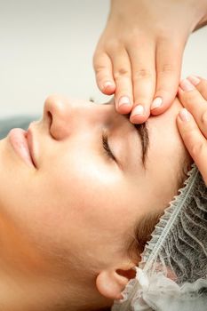 Young caucasian woman receiving facial massage by beautician's hands in spa medical salon