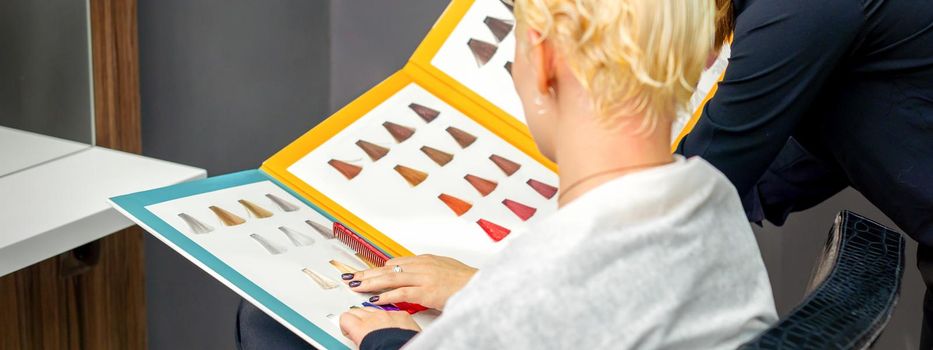 Professional female hairdresser and female client choosing hair dye color from hair color samples in a hair salon