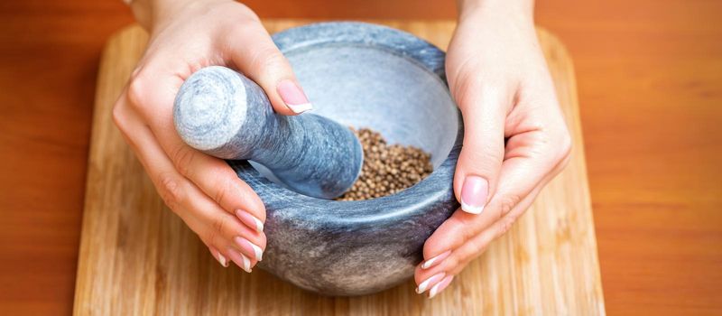 Female hands grind dry pepper spices in mortar on a wooden kitchen board