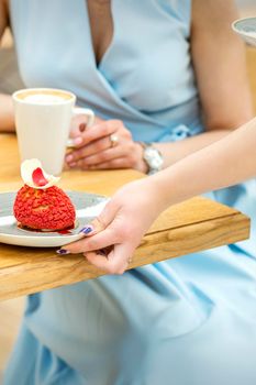 The waiter's hand puts on the table a plate with a red cupcake on the background of a female client in a cafe