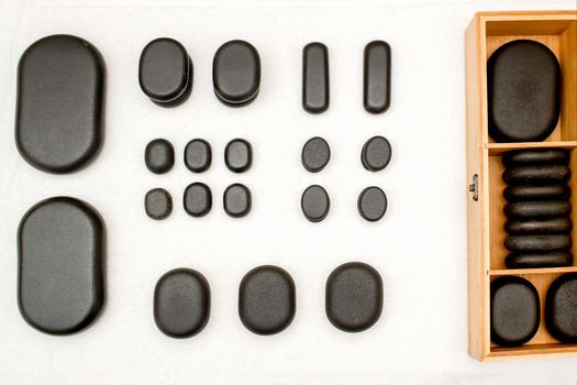 Flat lay of an open wooden case with spa black stones on a table in spa salon. Top view set of spa black stones