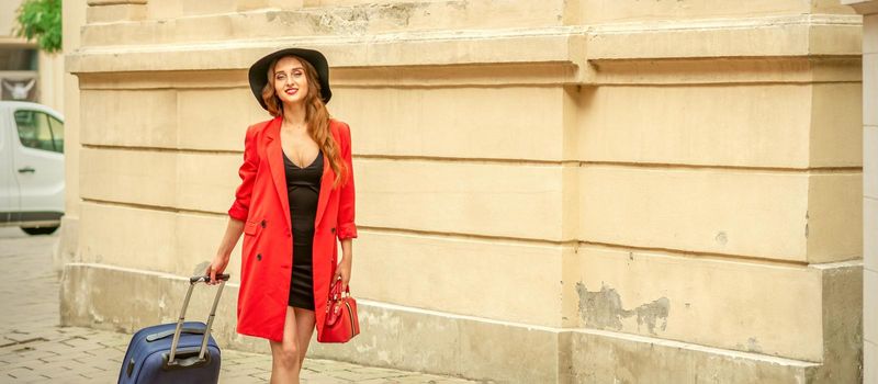 A beautiful young caucasian woman is walking with a suitcase on an old city street