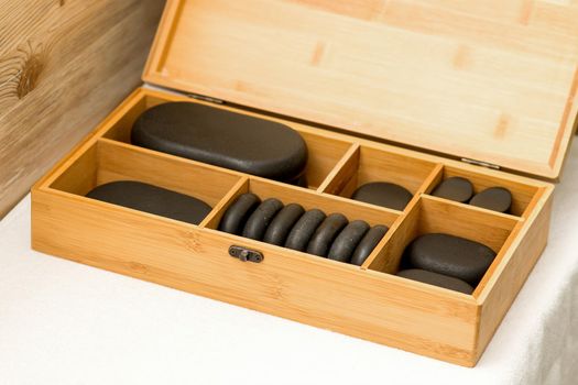 Close up of an open wooden case with spa black stones on a table in spa salon
