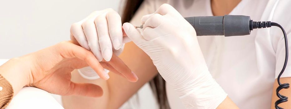 Closeup of manicure master removes nail polish uses an electric nail file in a nail salon