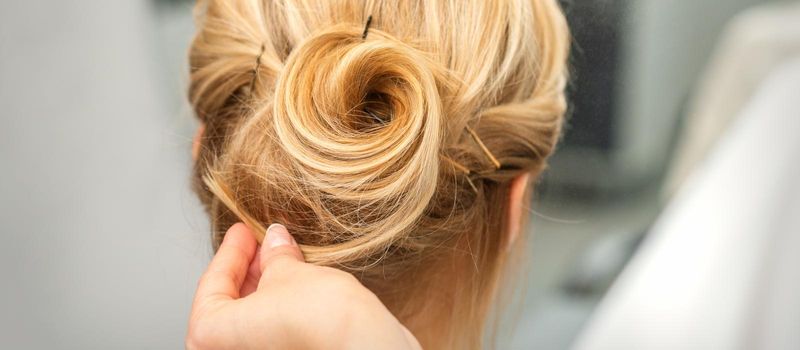 Close up of female hairdresser styling blonde hair of a young woman in a beauty salon