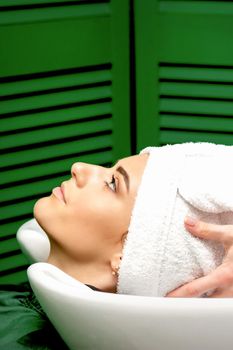 Side view of female hairdresser dries the female client's hair with a towel in the sink at a hair salon