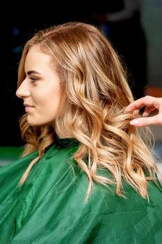 Side view of hands of female hairdresser styling hair of a blonde woman in a hair salon