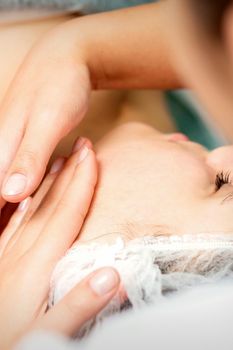 Young caucasian woman receiving facial massage by beautician's hands in spa medical salon