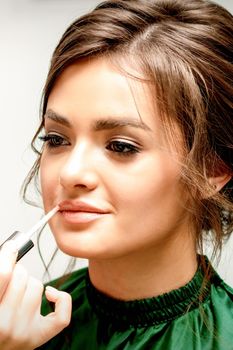 Close up of makeup artist applying lipstick foundation with a make-up brush on lips of the beautiful young caucasian woman in a beauty salon