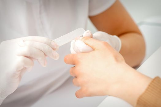 Close up of the hand of young woman receiving the nail file procedure in a beauty salon