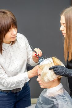 Two female hairdressers dyeing hair of young caucasian woman in hair salon