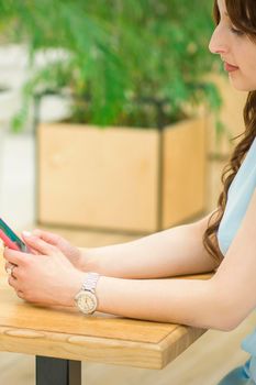 Beautiful young caucasian woman looking on smartphone sitting at the table outdoors