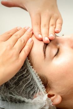 Young caucasian woman receiving facial massage by beautician's hands in spa medical salon