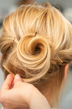 Close up of female hairdresser styling blonde hair of a young woman in a beauty salon