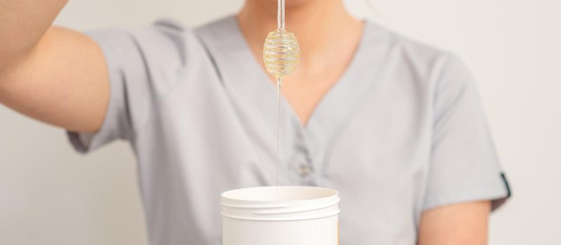 Beautician holding white bowl with wax flowing down from honey stick on a white background