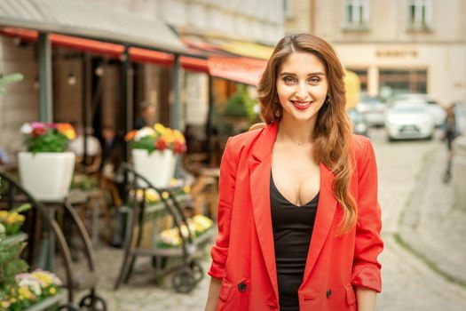 Portrait of a beautiful young caucasian woman smiling and standing on the city street looking at camera outdoors