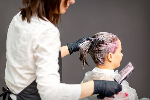 Female hairdresser dyeing hair of young caucasian woman in hair salon