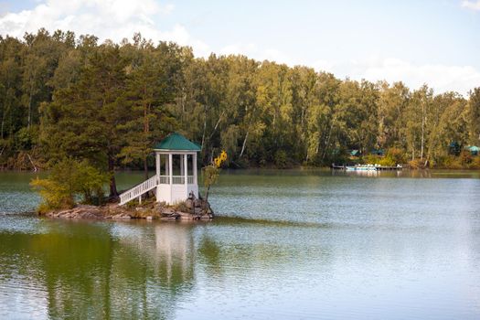 A small beautiful island on Lake Aya in the Altai Territory or the Altai Republic. There is a small gazebo on the island and a forest around the lake.