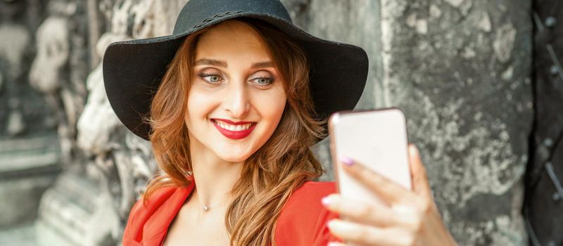 Close up of beautiful young caucasian woman taking selfie on smartphone standing and smiling against ancient building outdoors