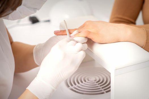 Close up of the hand of young woman receiving the nail file procedure in a beauty salon