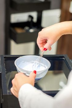 The hairstylist makes a white color dye mix for coloring hair at a salon close-up.