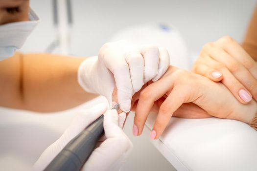 Manicure master applying electric nail file machine removing old nail polish on fingernails in a nail salon