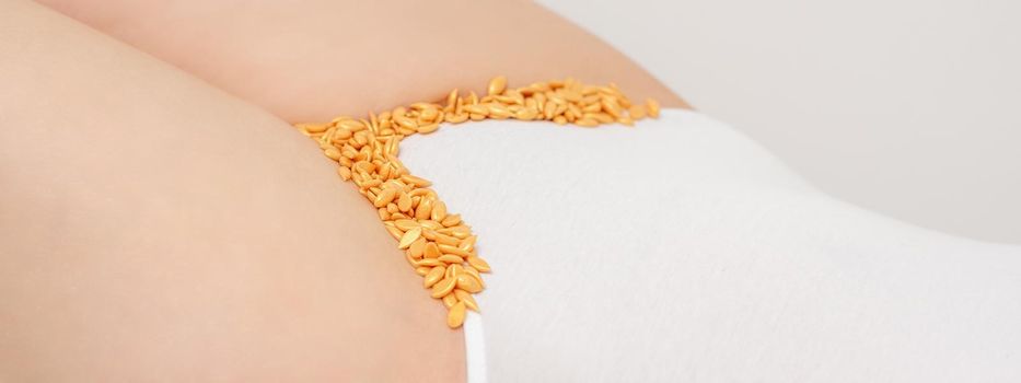 Depilation of the bikini area. Bikini zone of a young woman with wax hard beans lying down on a white background