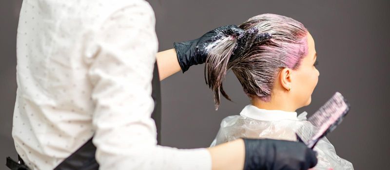 Female hairdresser dyeing hair of young caucasian woman in hair salon