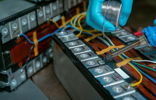 Technician use soldering iron to solder metal and wire of lithium-ion rechargeable battery. Repair module of Li-ion battery. Engineer hand holds soldering iron and tin-lead to solder electronic board.