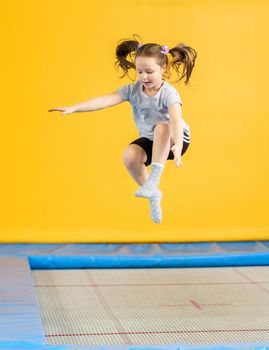 Happy child girl jumping on trampoline in fitness center