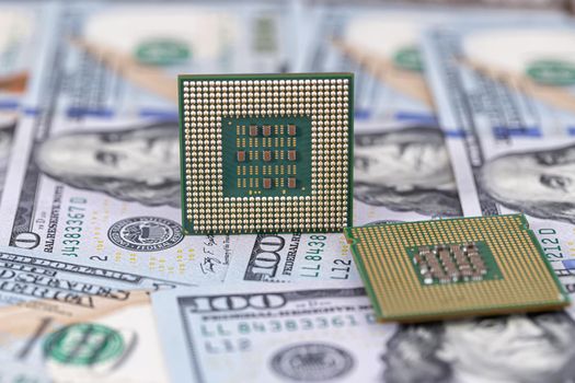 Two old computer processors lie in a pile of hundred-dollar bills