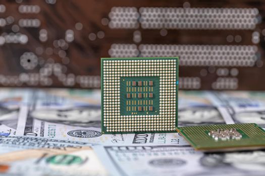 Two old computer processors lie in a pile of hundred-dollar bills