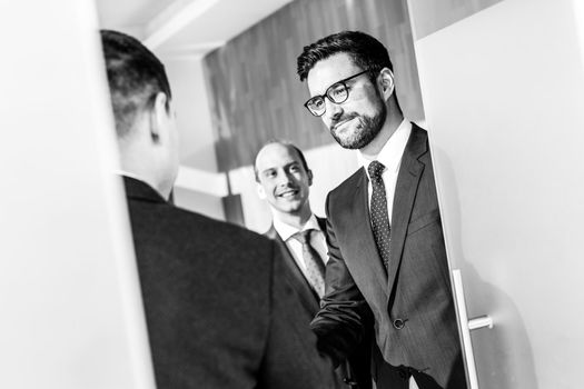 Group of confident business people greeting with a handshake at business meeting in modern office. Closing the deal agreement by shaking hands. Black and white image.