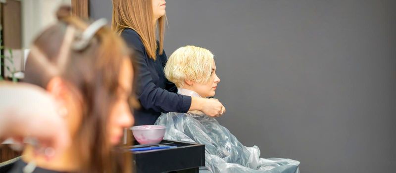 The female hairdresser puts on a transparent cellophane cape to the female client in a beauty hair salon