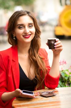 Portrait of a beautiful young smiling caucasian woman sitting at the table with a cup of coffee in a cafe outdoors