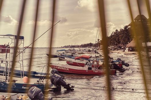Playa del carmen, Mexico 20 august 2022: View filtered by palm leaves of an array of small fishing boats moored on the beach of Playa del Carmen in Mexico.