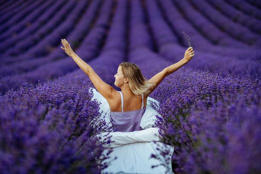 A middle-aged woman sits in a lavender field and enjoys aromatherapy. Aromatherapy concept, lavender oil, photo session in lavender.