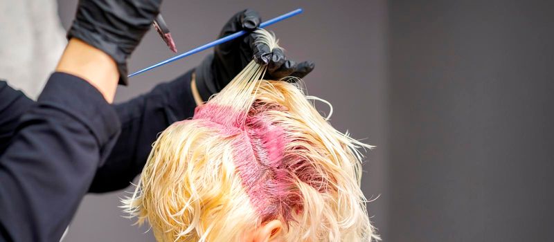 Close up of hairdresser's hands applying pink dye on woman's blonde hair at a hair salon