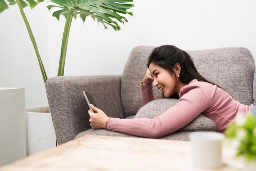 Happy young asian teen girl sit on sofa at home holding phone looking at screen waving hand video calling distance friend online in mobile