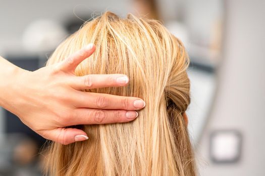 Close up of female hairdresser styling blonde hair of a young woman in a beauty salon