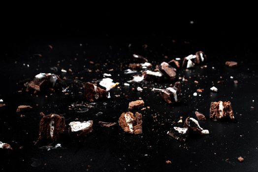 Scattered crumbs of chocolate sandwich cookies filled with sweet cream flavored isolated on black background