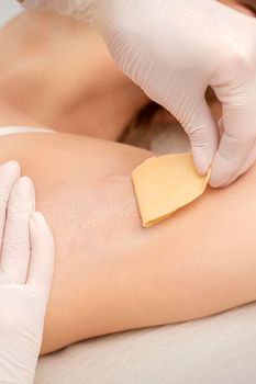 Close up of hands in gloves of beautician waxing young female armpit with sugar paste in hair removal salon