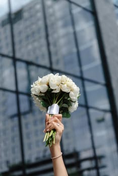 the bride holds the bouquet high above her head in front of the building.