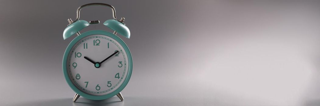 Close-up of single simple designed green retro clock on grey surface. Metal vintage clock on tiny legs stand. Time, timer, alarm, decor, rarity concept