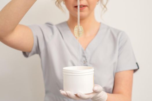 Beautician holding white bowl with wax flowing down from honey stick on a white background