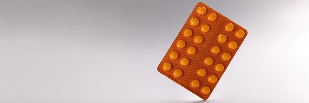 Close-up of blister with tablets, daily dose of medication for person. White tablets in orange package. Prescription, recovery, medicine, health concept