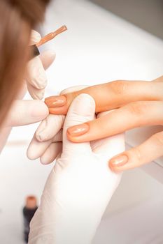 Manicurist applying beige nail polish on fingernails of a female client in a nail salon