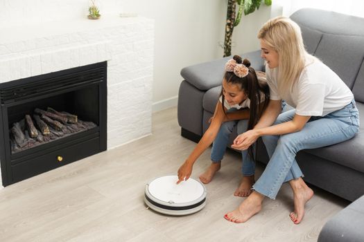 Young family resting on the couch while robotic vacuum cleaner doing its work at home. Household robots concept