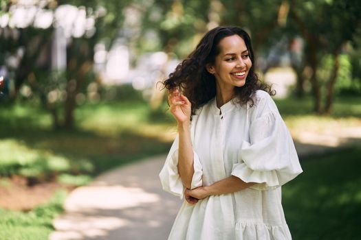 Portrait of a beautiful curly-haired brunette girl in the park. Girl smiling and holding her hair. High quality photo