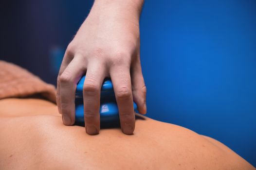 The concept of a healthy body. Hand putting a blue rubber jar for massage on a man's back. Close-up.